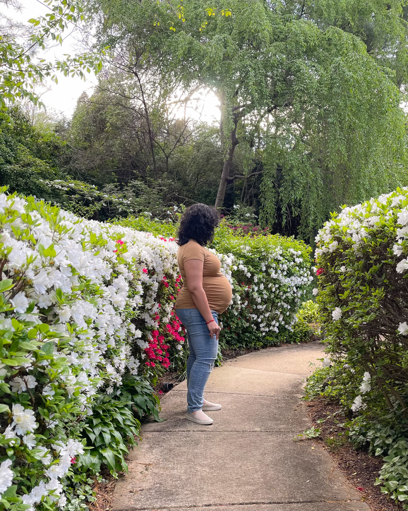 portrait of a 39 weeks pregnant woman standing with white and pink flowers behind her